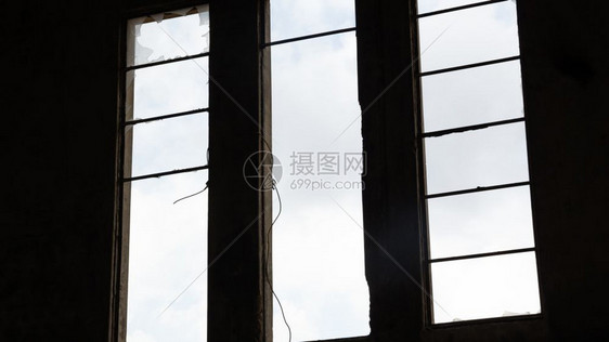 一个废弃建筑的破碎窗口从内部查看天空窗外看到云层图片