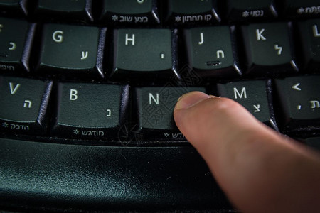 男人在无线键盘上打字用希伯来语和英字母打按新钮顶视图黑暗气氛图片