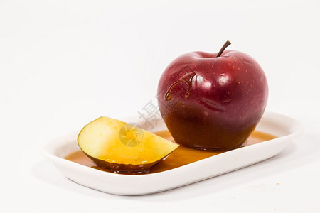 红苹果和切片白盘上有一滴蜂蜜白色背景是孤立的蜂蜜犹太新年的符号RoshHashanah图片