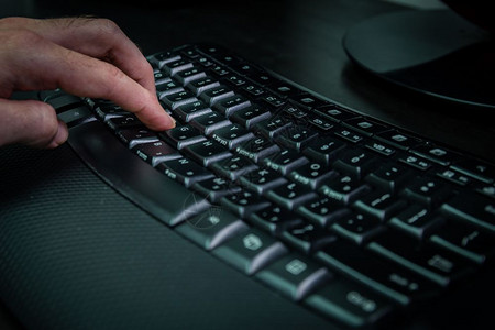 在键盘上打字的人用希伯来语和英字母打无线键盘黑暗气氛图片