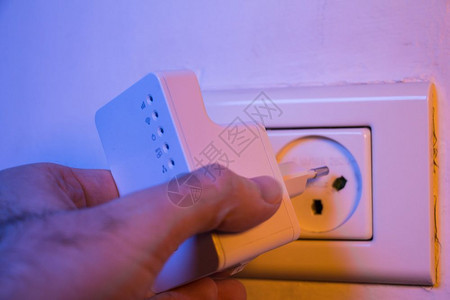 man在墙上的电插座入WiFi中继器该设备有助于扩展家庭或办公室的无线网络图片