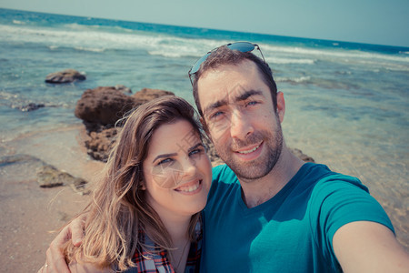 年轻夫妇在海滩上带着智能手机或相自拍图片