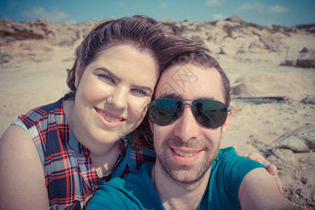 年轻夫妇在海滩上带着智能手机或相自拍图片