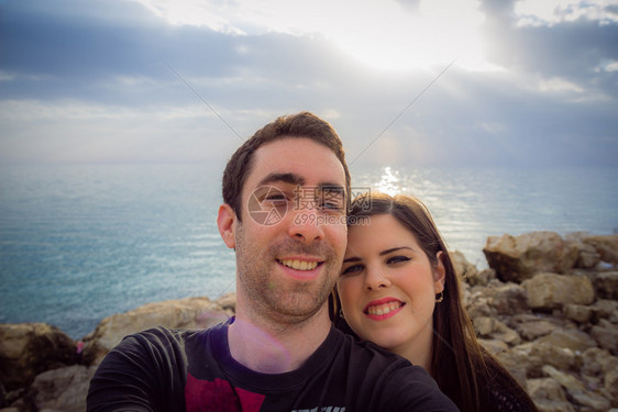 快乐的一对情侣在日落海岸背景中带着智能手机或相自拍图片