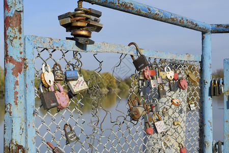 新婚夫妇和恋人挂在河边的栅栏上爱锁是牢固关系和永恒爱的象征俄罗斯克拉诺达尔2017年月4日新婚夫妇和恋人挂在河边的栅栏上爱锁牢固图片