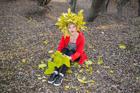 这女孩坐在秋叶树丛中穿着红色夹克有黄秋叶花圈的女孩秋叶皇后小姐季散步叶树丛中黄色秋叶花圈的女孩秋叶王树丛女孩坐在秋叶树丛中她坐在图片