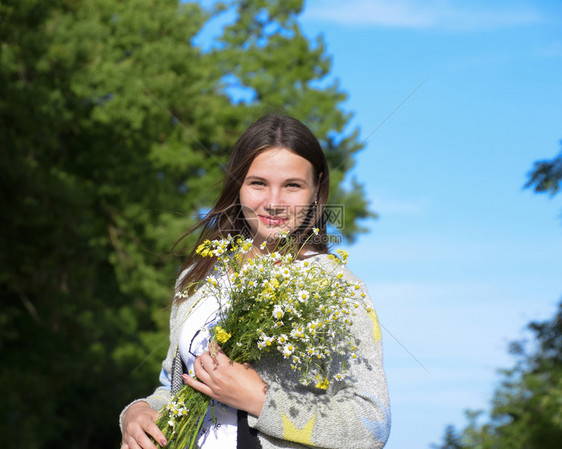 女孩站在森林里拿着一束甘菊花图片