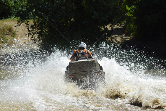ATV上的人横过一条溪流旅游者在跨国的地形上行走图片