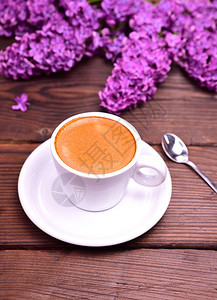 一杯白色的咖啡里配着碟子和勺放在一束紫色的花后面最顶端的风景图片