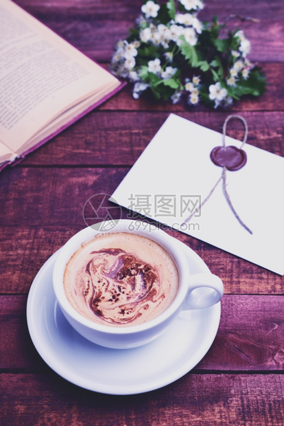 喝棕色桌上的热咖啡卡布奇诺藏在一本开着的书和束白花后图片