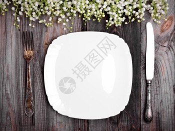 白瓷板灰色木制桌布上有铁旧餐具装饰着山谷白百合花顶视图片