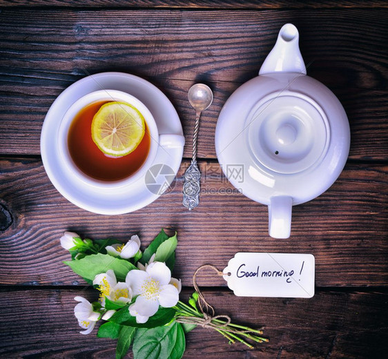 黑茶加柠檬和白壶旁边的一束花朵茉莉和纸标签顶端的景色图片