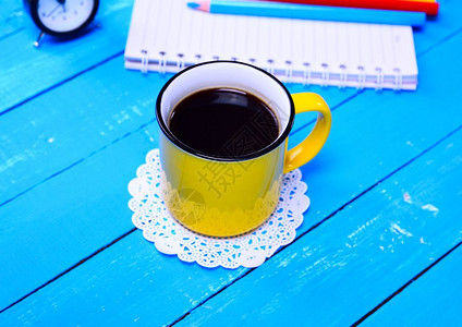 蓝色木头背景的黄杯黑咖啡图片