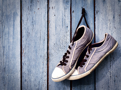 一对老人的肮脏蓝色运动鞋挂在空旷的木墙上图片
