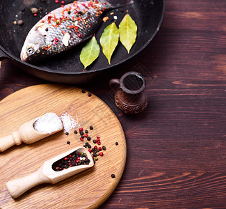 在黑煎锅和含胡椒盐的黑煎锅中捕食鱼用胡椒做木本底的烹饪菜图片