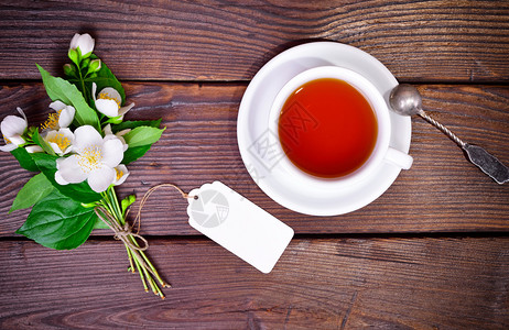 白黑茶杯碟和铁勺在棕色木制桌子上旁边一束花朵茉莉图片