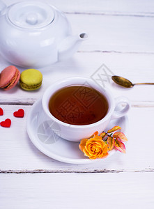红茶放在一个白色的圆形杯子里茶碟放在白色的木制背景上在一个白色的茶壶后面图片