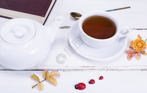 红茶放在一个带茶碟的圆形白色杯子里旁边是一个白色茶壶和一本合上的书图片