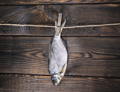 咸鱼羊被挂在一根绳子上挂在棕色木头背景上图片