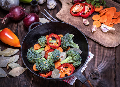 棕色桌上的黑铁煎锅里新鲜的西兰花胡萝卜和红辣椒图片