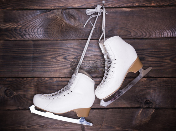 女白人用过的皮溜冰鞋挂在棕色木背景的钉子上图片