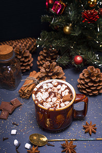 黑色背景和圣诞装饰的棕色陶瓷杯中带有棉花糖片的热巧克力图片