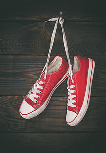 一对红色的旧运动鞋挂在钉子上棕色木墙的背景上图片