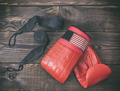 棕色木背景的红皮拳击手套和黑绷带图片