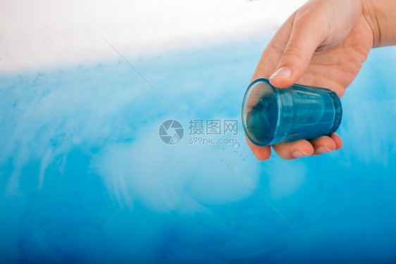 手握着从蓝色玻璃中倒下的水图片
