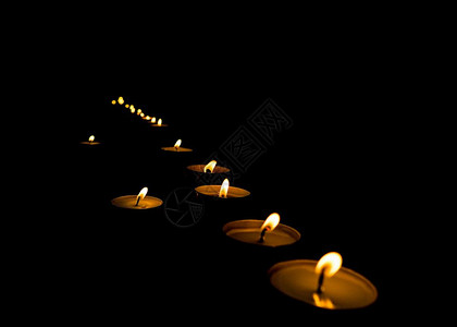 在黑暗中点燃蜡烛在黑暗中闪烁的教堂里点燃的祈祷蜡烛的火焰图片