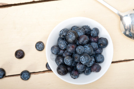 一碗新鲜的蓝莓边有银勺子放在木桌上图片