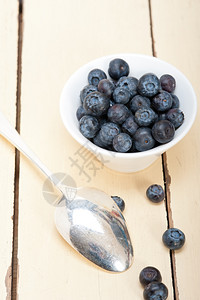 一碗新鲜的蓝莓边有银勺子放在木桌上背景