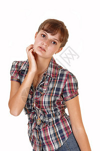 一个美丽的十几岁女孩站在工作室拿着她的头用一只手在个格斗上衣白色背景图片