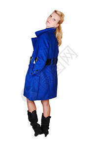 一个穿着蓝色冬大衣和黑靴的漂亮高个子女人站在工作室手放口袋里仰望着肩膀寻找白背景图片