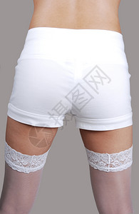 一个穿白短裤和袜的年轻女子站在背面摇欲坠的屁股寻找浅灰色背景图片