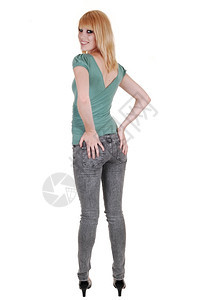 一个穿牛仔裤和绿色毛衣的漂亮又高个子年轻女人站在工作室后面拿着她的屁股站在白背景上图片