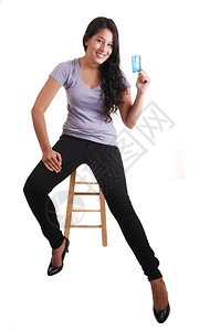 一位高个子的年轻女坐在椅上手里拿着她的第一张信用卡长发黑和牛仔裤白底衣背景图片