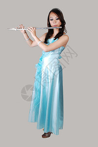 一位年轻的亚洲女人穿着淡蓝色的晚礼服在工作室的地板上吹长笛以浅灰色背景图片