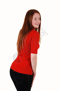 一个站在背面的年轻可爱女人看着她的肩膀穿一件红色毛衣和牛仔裤长着红色头发白背景图片