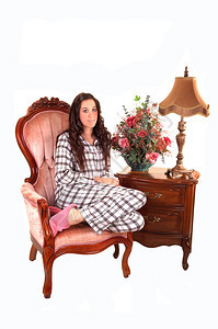 一个穿着睡衣的年轻美女坐在粉红色的扶手椅上和一个床头柜白底灯图片
