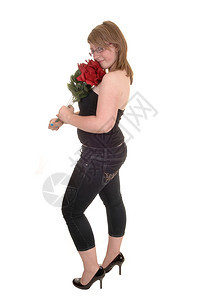 一个年轻美女站在白色背景的侧面手里拿着红玫瑰穿牛仔裤和高跟鞋图片