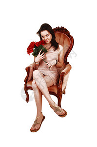 一位美丽的年轻女士坐在粉红色的椅子上穿着美色洋装拿一束红玫瑰白色背景图片