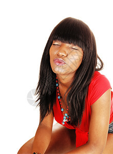 一个美丽的年轻黑人女穿着红色上衣长的黑头发白背景并闭上眼睛亲吻图片
