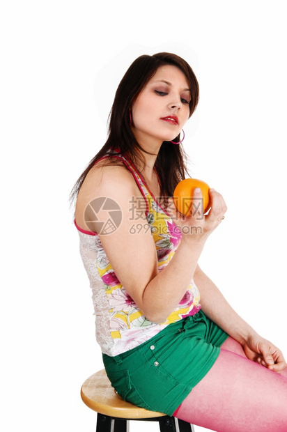 一位年轻女坐在绿短裤和长袍上坐在椅子手里拿着黄色橙与白种背景隔绝图片