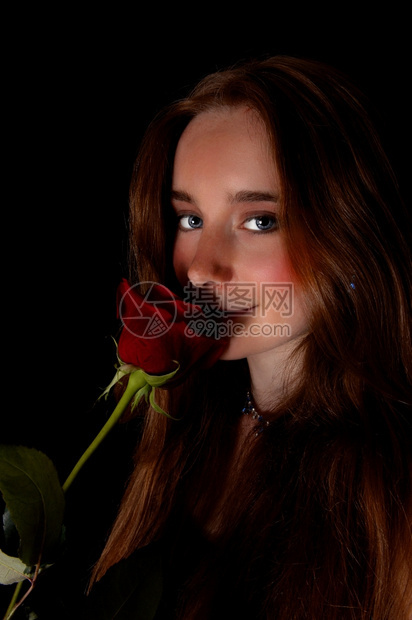 一位美丽的年轻女站在黑人背景拿着红玫瑰对她的脸看镜头图片