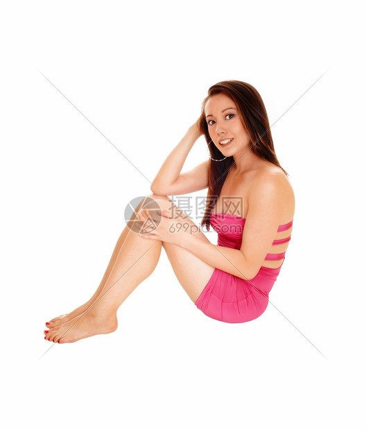 一个可爱的年轻亚洲女人穿着短的粉红色裙子坐在地板上微笑着被白种背景隔绝图片