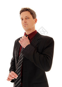 一个商人站在西装修补他的领带看着严肃孤立的白色背景图片