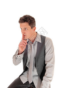 一个穿着灰色衬衫和背心的年轻人坐在白色背景上嘴沾满了手指图片