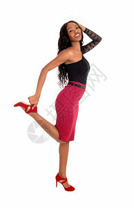 一个可爱的非裔美国女人穿着红裙子和黑色上衣抬起她的腿微笑着与白背景隔绝图片