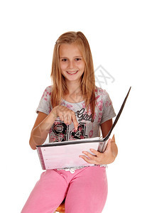 一个笑着的金发年轻女孩穿着粉红色的裤子拿着皮夹指她的工作与白种背景隔绝图片